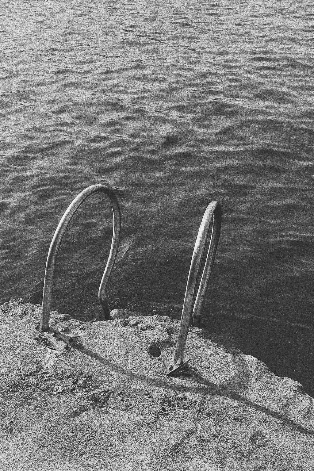 black and white metal ladder descending into calm water at the edge of a stone pier